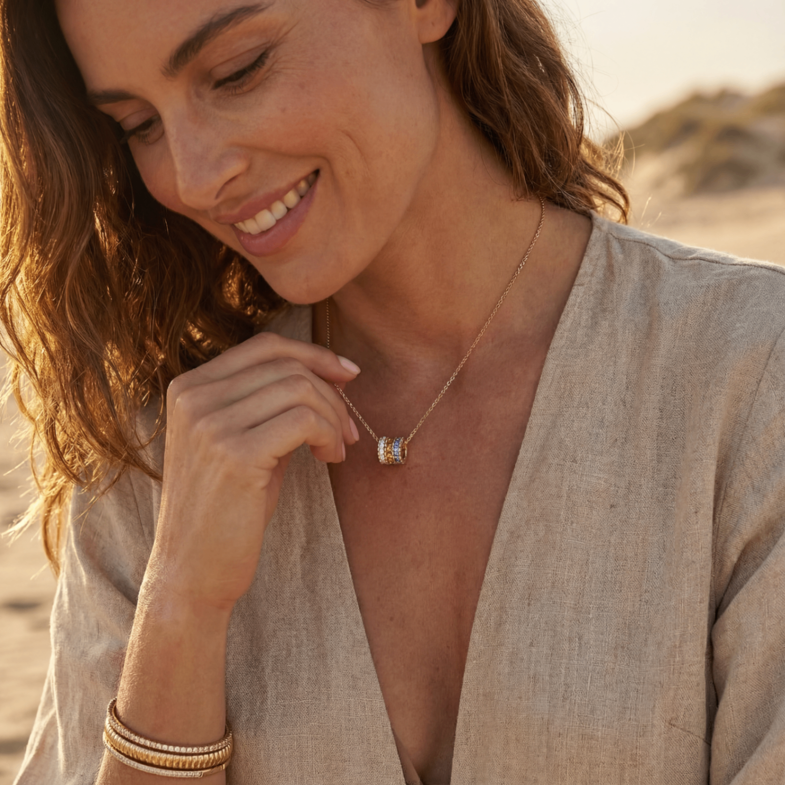 Smiling woman on beach wearing layered gold necklace and bracelets