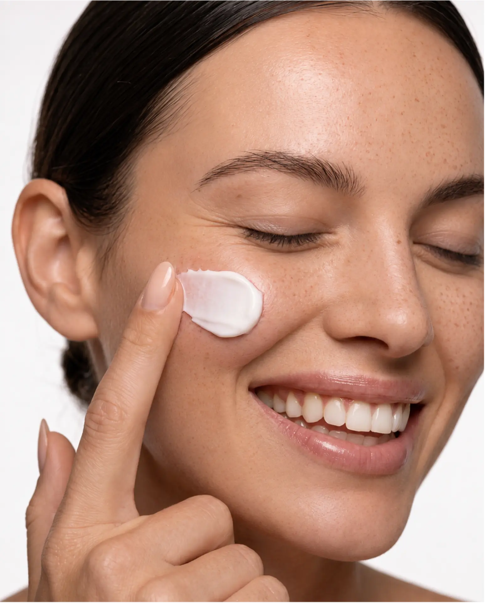 Close-up of a smiling model applying white face cream to her cheek